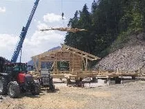 Kran hebt Holzteile auf die Baustelle eines Stalls, davor ein Traktor
